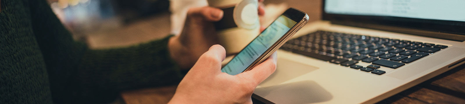 Close up of a person's hands holding a smartphone and a coffee cup